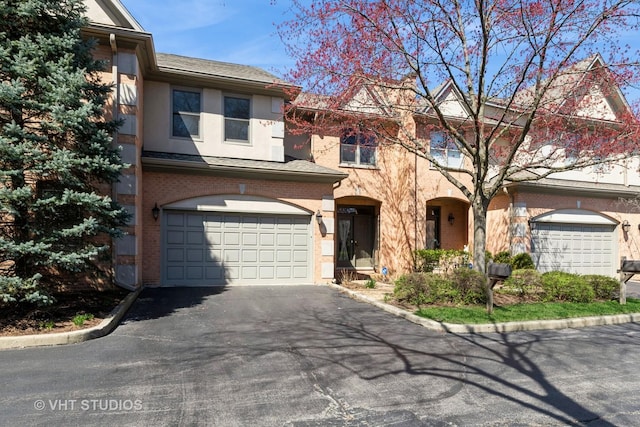 view of property featuring brick siding, an attached garage, driveway, and stucco siding