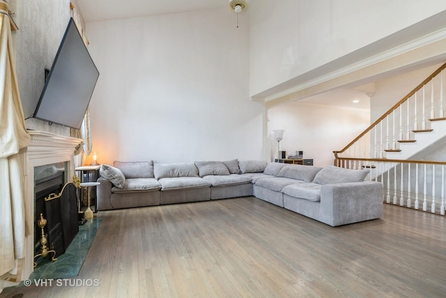 living area with a fireplace, stairway, a towering ceiling, and wood finished floors