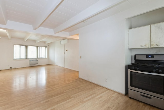 kitchen with a wall mounted AC, stainless steel gas range, light wood-type flooring, white cabinetry, and beamed ceiling