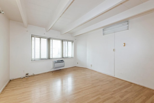 empty room with a wall mounted AC, light wood finished floors, and beam ceiling