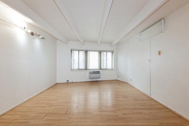 spare room featuring beam ceiling, light wood-style flooring, and a wall unit AC