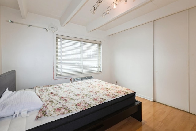 bedroom with light wood-style floors, a closet, and beam ceiling