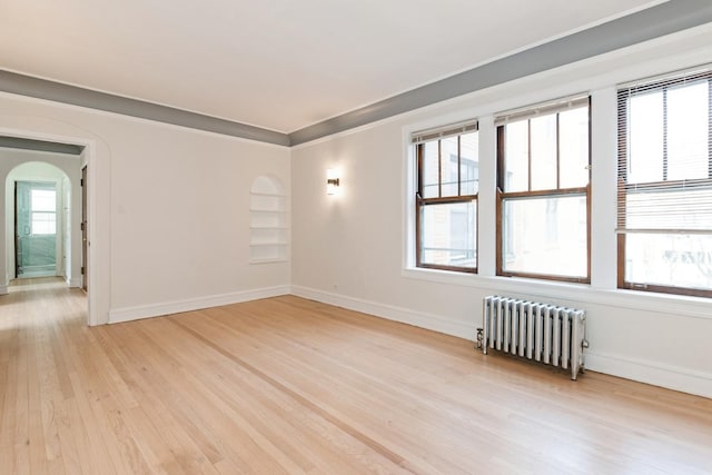 spare room featuring light wood-type flooring, baseboards, crown molding, radiator heating unit, and arched walkways