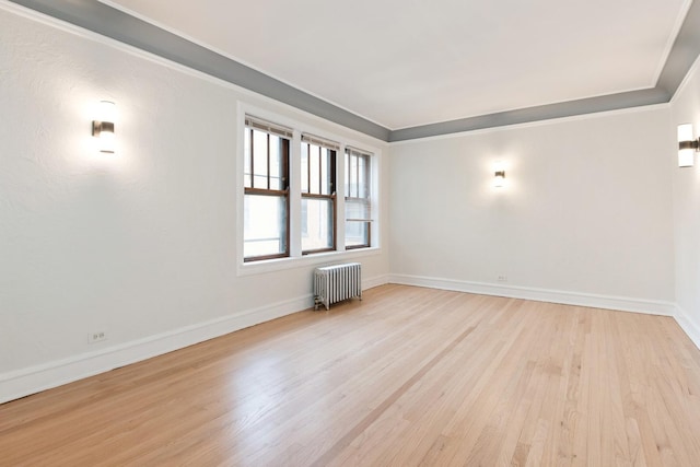 empty room with crown molding, radiator heating unit, baseboards, and light wood-style floors