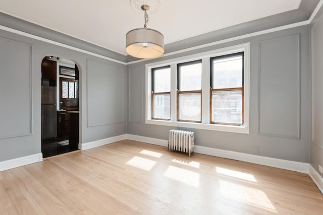 unfurnished room with arched walkways, radiator, light wood finished floors, and baseboards