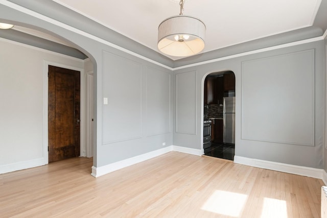 empty room featuring a decorative wall, baseboards, light wood-type flooring, and arched walkways