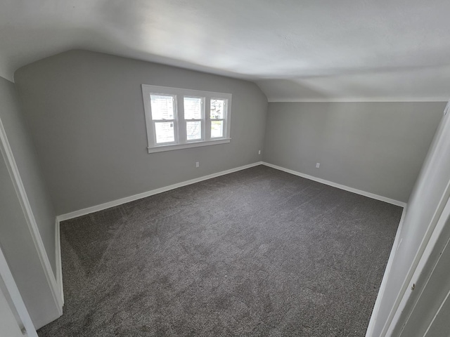 additional living space featuring baseboards, dark colored carpet, and vaulted ceiling