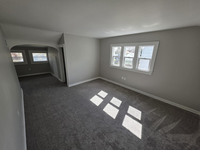 unfurnished room with dark carpet, arched walkways, and baseboards