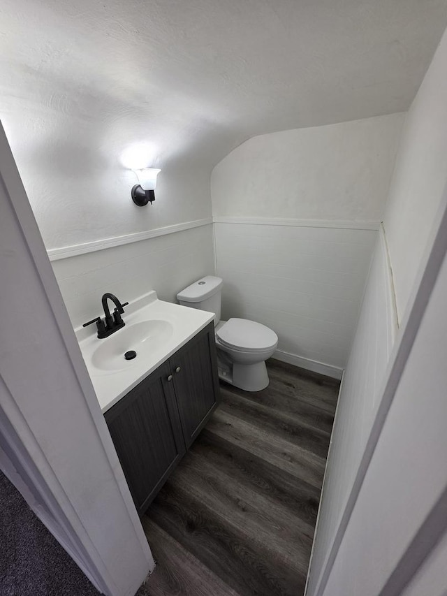 half bath with vanity, vaulted ceiling, toilet, and wood finished floors