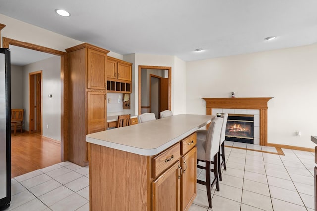 kitchen featuring light tile patterned floors, a fireplace, a center island, light countertops, and a breakfast bar area