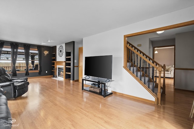 living area featuring a fireplace with flush hearth, wood finished floors, baseboards, and stairs