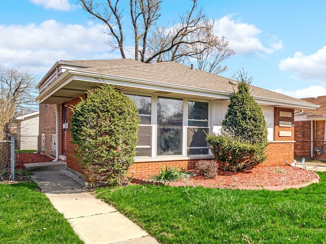 view of front of property with brick siding, fence, roof with shingles, and a front yard