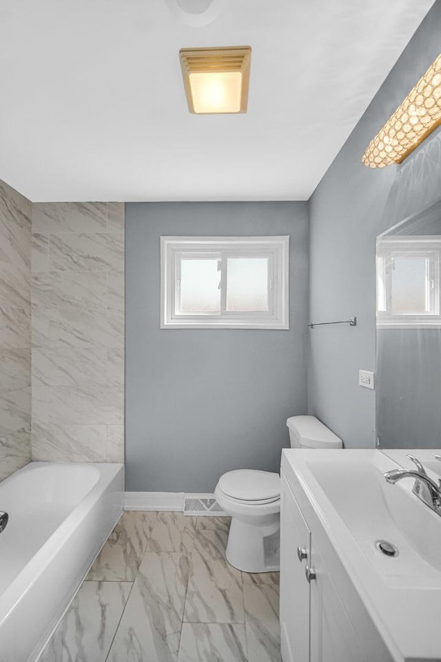 bathroom with a healthy amount of sunlight, a bathtub, marble finish floor, and toilet