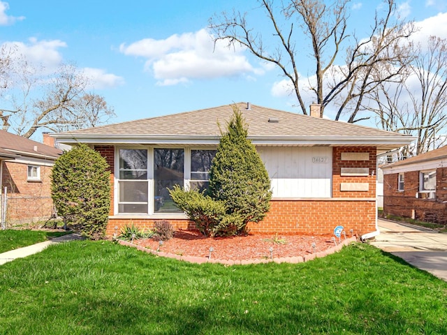 rear view of house with a chimney, a shingled roof, brick siding, a lawn, and a sunroom