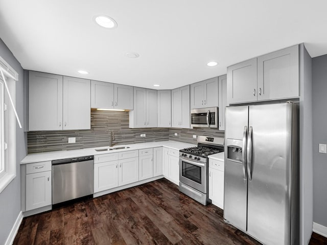 kitchen with stainless steel appliances, a sink, backsplash, gray cabinetry, and light countertops