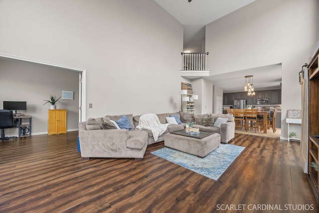 living area featuring a towering ceiling, dark wood finished floors, a chandelier, and baseboards