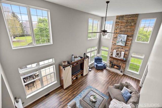 living room with plenty of natural light, a fireplace, ceiling fan, dark wood finished floors, and a towering ceiling