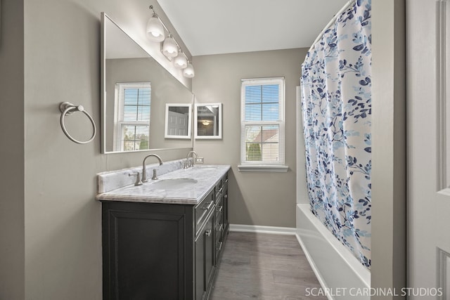 bathroom with baseboards, wood finished floors, double vanity, and shower / tub combo with curtain