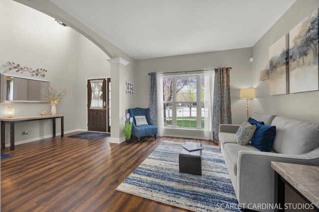living area featuring arched walkways, wood finished floors, baseboards, and decorative columns