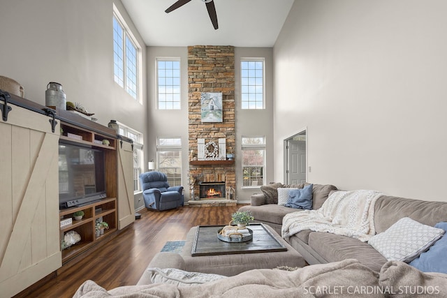 living area featuring ceiling fan, high vaulted ceiling, wood finished floors, and a stone fireplace