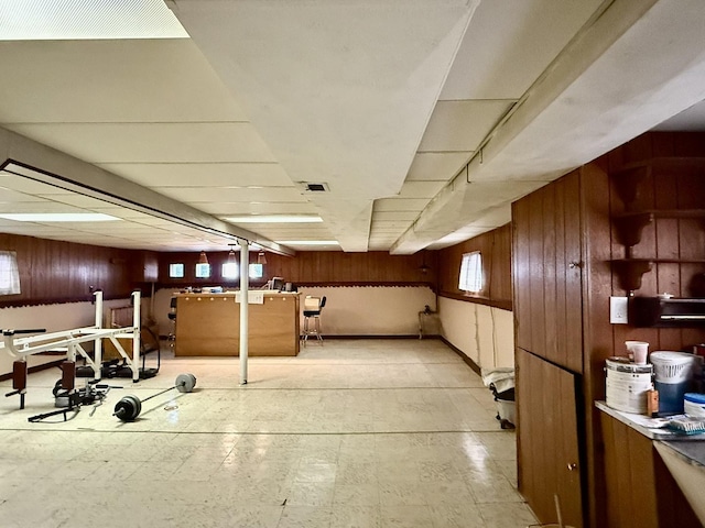 basement featuring a paneled ceiling, wooden walls, and light floors