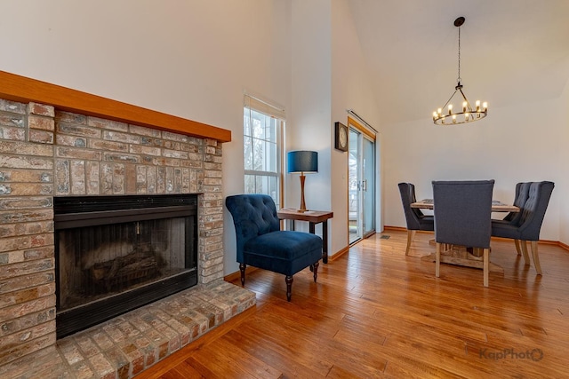 dining space with an inviting chandelier, a fireplace, a towering ceiling, wood finished floors, and baseboards