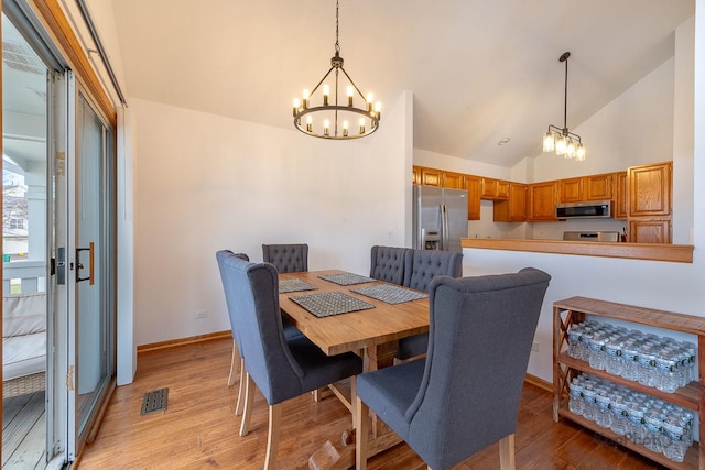 dining area with high vaulted ceiling, an inviting chandelier, visible vents, light wood finished floors, and baseboards