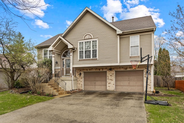raised ranch featuring fence, a shingled roof, brick siding, a garage, and aphalt driveway