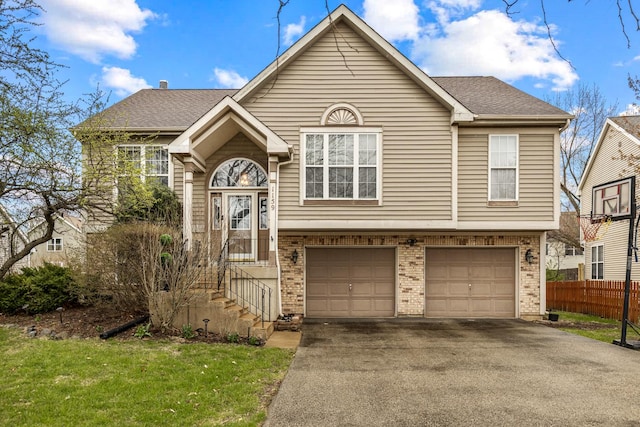 split foyer home featuring a garage, fence, brick siding, and aphalt driveway