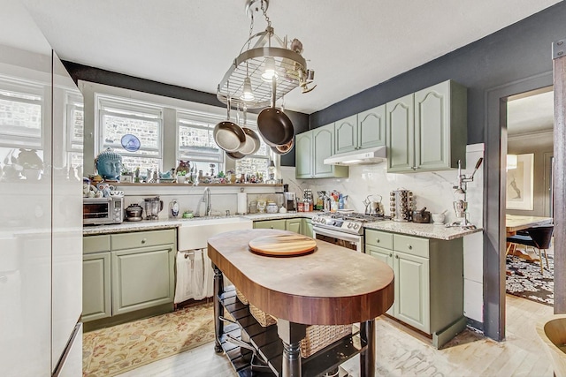 kitchen featuring gas range, a sink, under cabinet range hood, backsplash, and light wood-style flooring