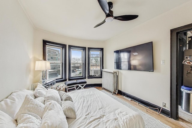 bedroom featuring baseboards, ornamental molding, a ceiling fan, wood finished floors, and radiator heating unit