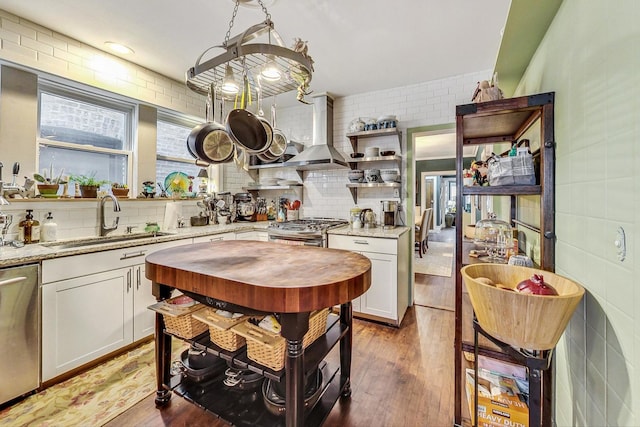 kitchen with a sink, wall chimney range hood, white cabinetry, stainless steel appliances, and light wood-style flooring