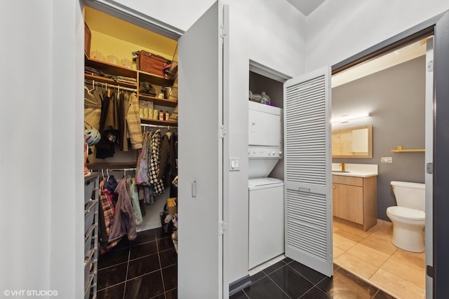 bathroom featuring toilet, stacked washing maching and dryer, a walk in closet, vanity, and tile patterned flooring