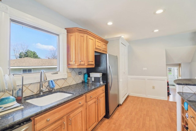 kitchen with dark stone counters, decorative backsplash, stainless steel appliances, light wood finished floors, and a sink