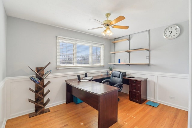 home office with a decorative wall, wainscoting, light wood-type flooring, and ceiling fan