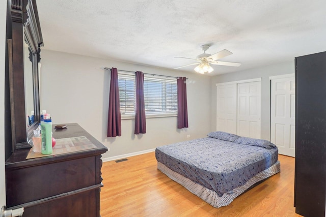 bedroom with baseboards, light wood-style flooring, two closets, visible vents, and ceiling fan