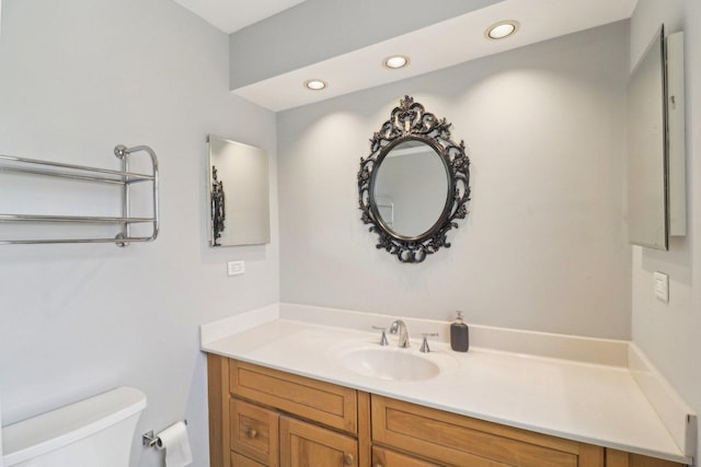 half bathroom featuring recessed lighting, vanity, and toilet