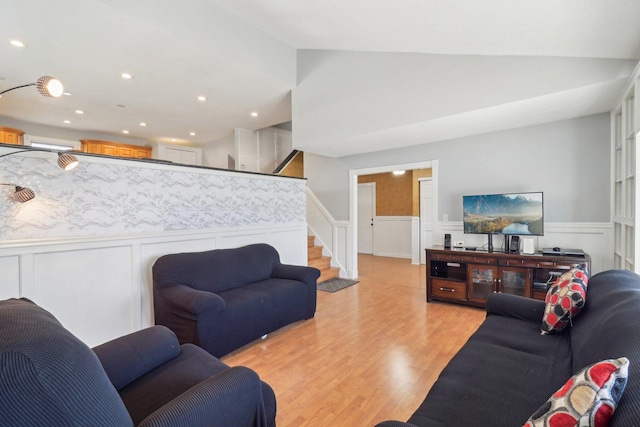 living area with a decorative wall, light wood-type flooring, recessed lighting, wainscoting, and stairs