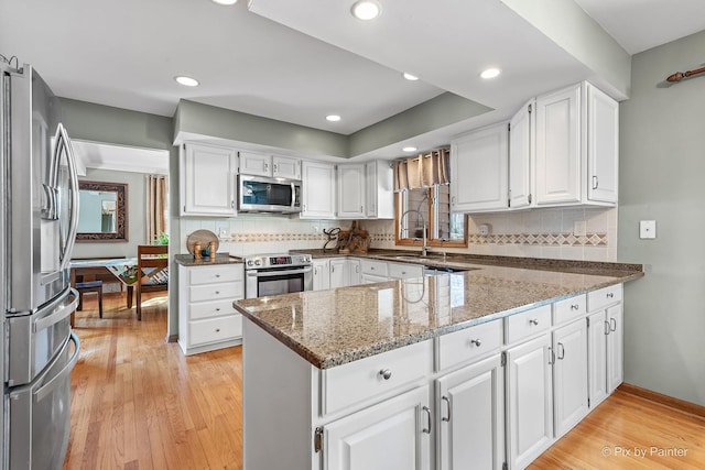 kitchen with light wood finished floors, a peninsula, white cabinets, and appliances with stainless steel finishes