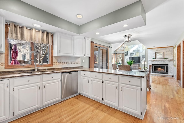 kitchen with a peninsula, white cabinets, stainless steel dishwasher, light wood finished floors, and a sink