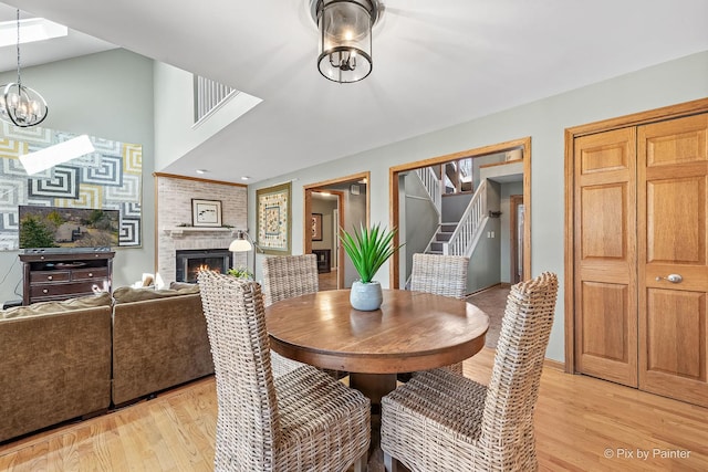 dining area featuring light wood-type flooring, a notable chandelier, stairway, and a fireplace