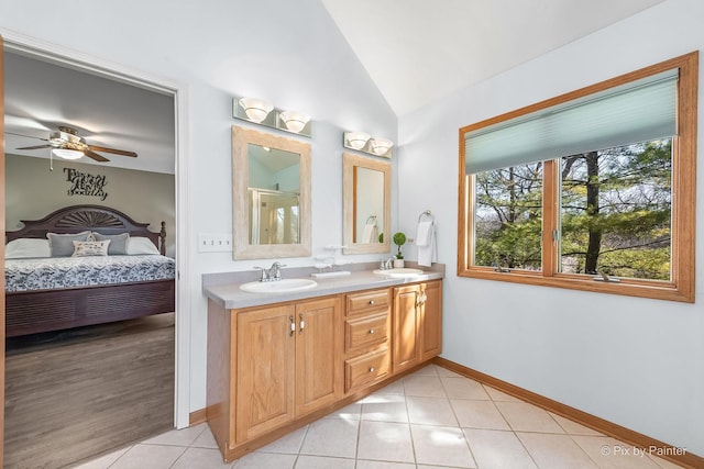 ensuite bathroom featuring tile patterned floors, double vanity, a sink, and lofted ceiling