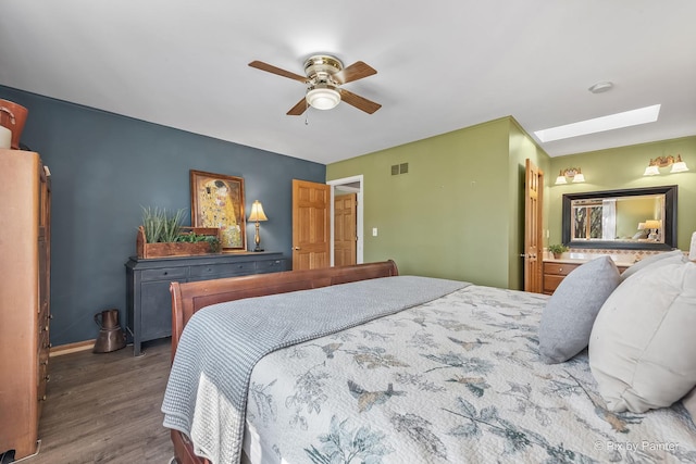 bedroom with a ceiling fan, visible vents, a skylight, wood finished floors, and baseboards