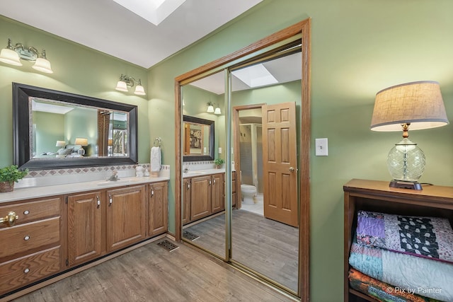 bathroom featuring two vanities, a sink, toilet, and wood finished floors