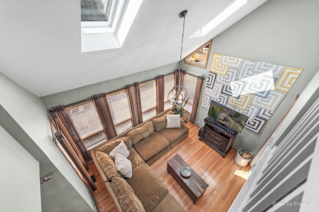 living area with vaulted ceiling with skylight, wood finished floors, and an inviting chandelier