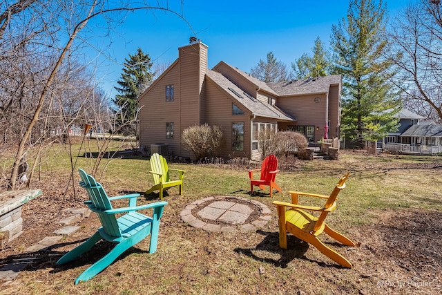 rear view of property with central AC, a chimney, a fire pit, and a yard