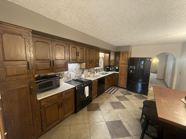 kitchen with light countertops, arched walkways, a textured ceiling, and black appliances