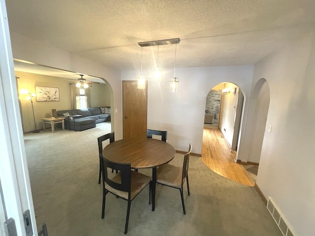 dining space featuring light colored carpet, arched walkways, a ceiling fan, and visible vents