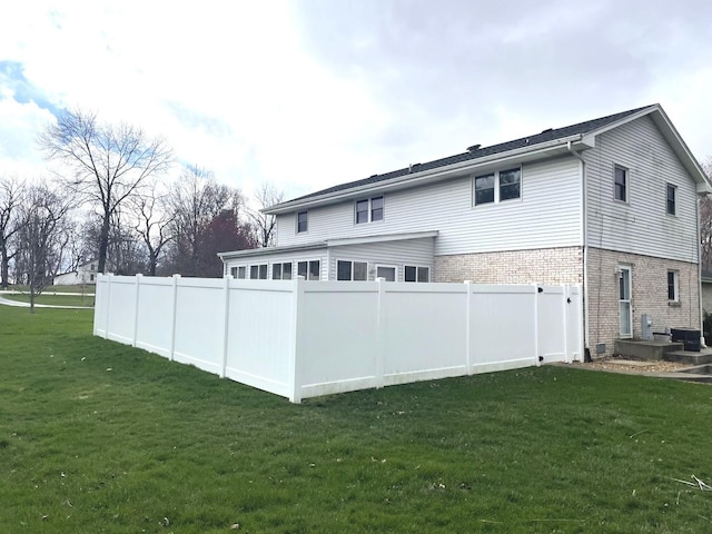 rear view of house featuring brick siding, central AC, fence, and a yard
