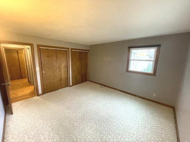 unfurnished bedroom featuring baseboards, carpet flooring, and multiple closets
